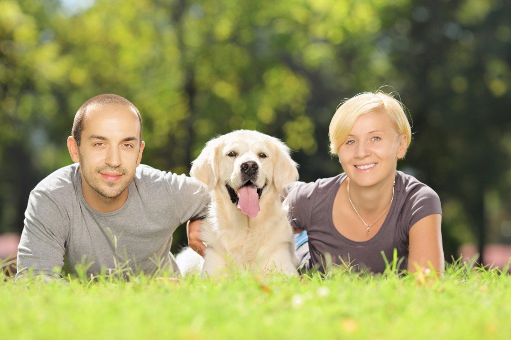 Smiling young couple lying on a grass and hugging a dog in a par