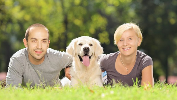 Smiling young couple lying on a grass and hugging a dog in a par
